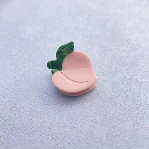 Close-up of a glossy pink peach-shaped acetate hair claw clip with green leaf detail