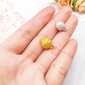 Macro shot of gold and silver magnetic jewelry clasps held in hand for size comparison