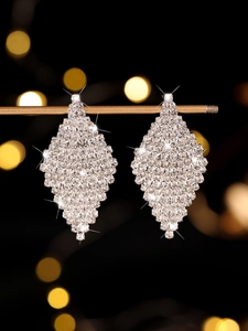 Macro detail of geometric silver earrings with sparkling white crystals on black background