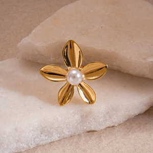 Macro shot of gold floral open ring with white pearl detail on textured stone