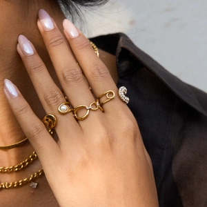 Gros plan sur une bague trombone en acier doré 18K et bijoux en perles portés en superposition