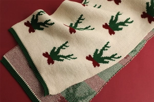 Detail of beige knit scarf with red and green Christmas deer patterns and plaid texture