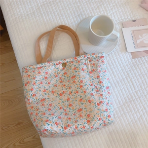 Detail of floral canvas lunch bag with khaki handles and gold button on quilted bed