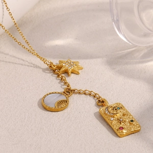 Detailed shot of 18K gold plated necklace with star, shell and eye charms on sand
