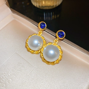 Detailed macro view of vintage faux pearl earrings with golden twisted edges and blue stones