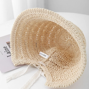 Detail of handwoven straw sun hat featuring scalloped edges and delicate white lace ties