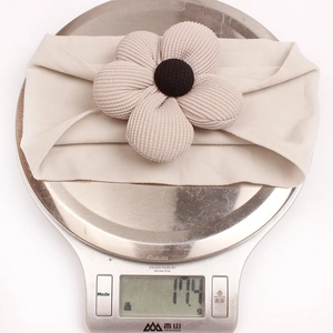 Detail view of 17.4g beige nylon floral baby headband with ribbed texture on scale