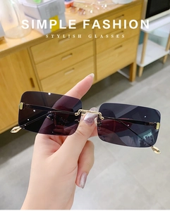 Detailansicht der lila randlosen Sonnenbrille mit goldenem Metallgestell in der Hand