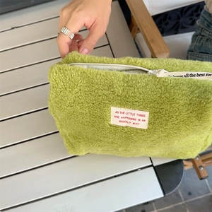 Close-up of soft green fleece makeup bag with white zipper and decorative woven strap