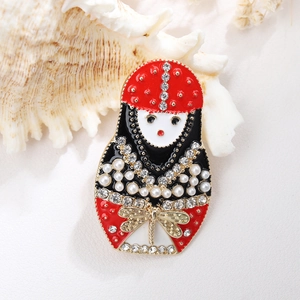 Macro detail of a Matryoshka doll brooch with red enamel, pearls, and rhinestones