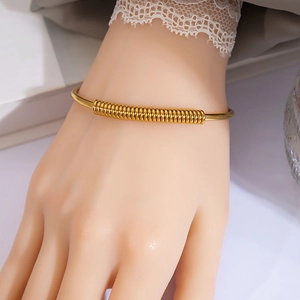 Detail of a gold metallic bangle with a spiral spring texture and minimalist design
