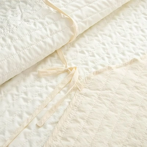 Close-up of cream white quilted fabric texture with soft ties for home bedding
