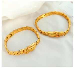 Detail shot of two gold belt-style titanium steel bracelets on white silk fabric
