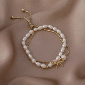 Detail of adjustable golden chain bracelet with freshwater pearls and a gold bow charm