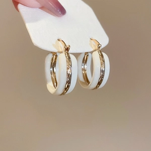 Detailed view of gold textured band on creamy white enamel hoop earrings with silver pins