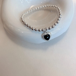 Detailed close-up of a silver beaded bracelet featuring a vintage black heart pendant