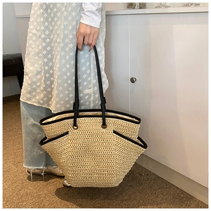Close-up of a large straw tote bag with black leather straps and woven texture details