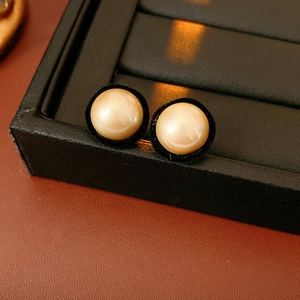 Macro view of champagne faux pearl stud earrings on a textured black jewelry tray