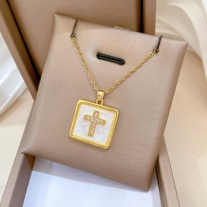 Close-up of golden square cross pendant with diamonds on white mother of pearl