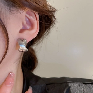 Close-up of minimalist silver X-shaped crossover stud earrings worn on the earlobe