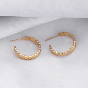 Detail of gold-plated twisted hoop earrings on white silk fabric with elegant texture