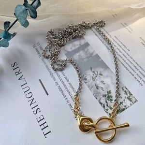 Detail of two-tone chain necklace with golden OT buckle on minimalist background