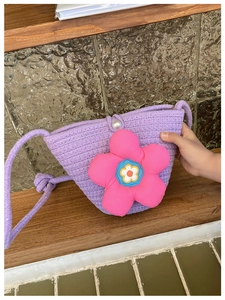 Detail der lila gewebten Strohtasche mit großer rosa Plüschblume und Perlenknopf