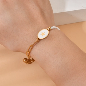 Close-up of golden paperclip chain bracelet with white beads and star pendant on wrist