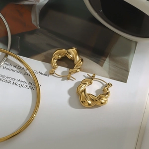 Detailed view of glossy 18k gold twisted hoop earrings on a fashion magazine