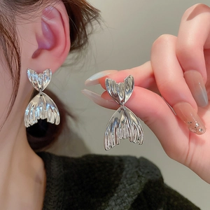 Close-up of silver fishtail dangle earrings showing textured metallic finish and ear fit