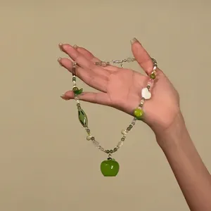 Détail d'un collier de perles avec un pendentif pomme verte et des perles de cœur