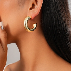 Close-up of elegant gold C-shaped hoop earring worn by a model on a neutral background