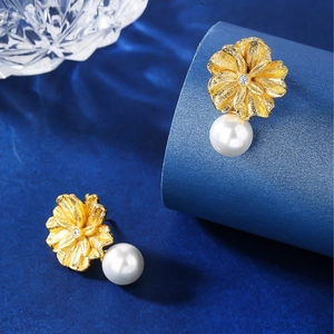 Elegant gold flower earrings with white pearl pendants and zircons on blue background