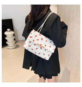 Détail de la texture d'un sac blanc en maille avec imprimé fraise et bandoulière chaîne