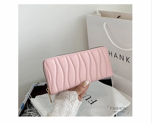 Detail of pink quilted wallet with wavy pattern and golden zipper held in hand