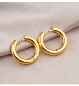 Macro shot of polished thick gold hoop earrings on elegant silk fabric background