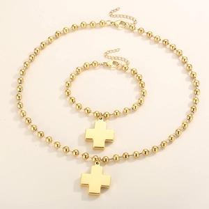 Flat lay of 18K gold bead necklace and bracelet set with cross pendants on beige background