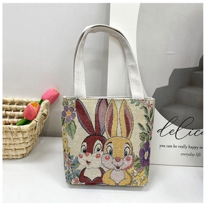 Detail of embroidered canvas tote bag with bunny pattern and floral accents on white table