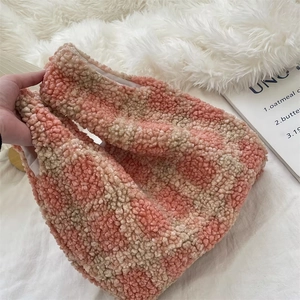 Detail of pink and beige checkered faux shearling tote bag on soft white plush surface