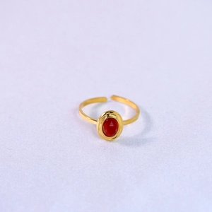Macro shot of gold plated open ring featuring an oval red natural stone on purple fabric