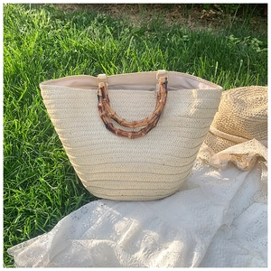 Detail of a large straw tote bag with bamboo handles on a white lace cloth