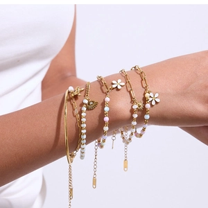 Détail de bracelets dorés superposés avec perles colorées et breloques de fleurs