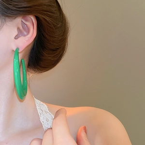 Detail view of large green resin C-hoop earring showing glossy finish on female model