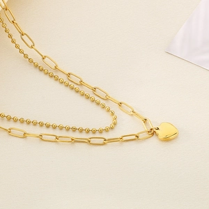 Detailed macro shot of a gold double-layer necklace featuring paperclip chain and heart pendant