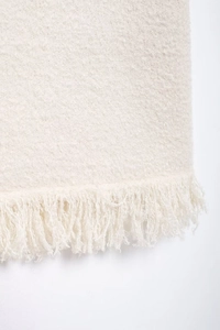 Detailed close-up of cream knit fabric texture with elegant fringe hem decoration