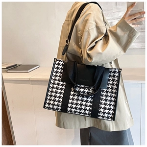 Detail view of large houndstooth tote bag with leather straps on model's shoulder