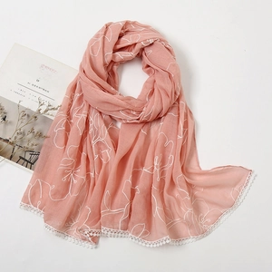 Detail of embroidered floral lace trim on a dusty rose linen scarf with white flower patterns