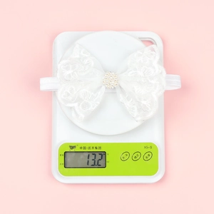 Detailed view of baby white lace bow headband weighing 13.2g on an electronic scale