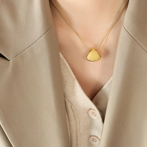 Elegant gold shell pendant necklace with ribbed texture on model in chic attire