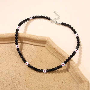 Close-up of beaded necklace with red heart charms and black beads on a textured tray